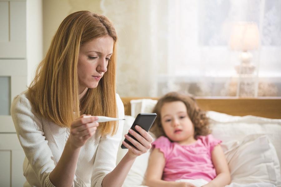 mom with sick daughter using her phone to call doctor